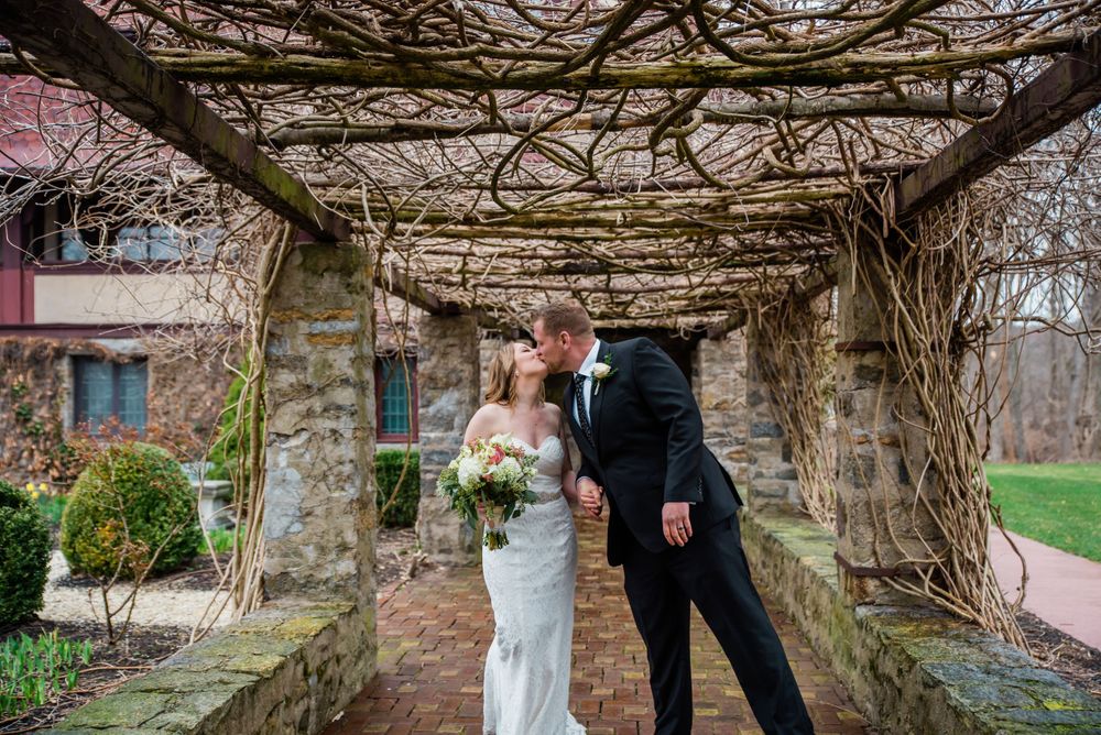A romantic moment captured beneath a vine-covered stone colonnade.