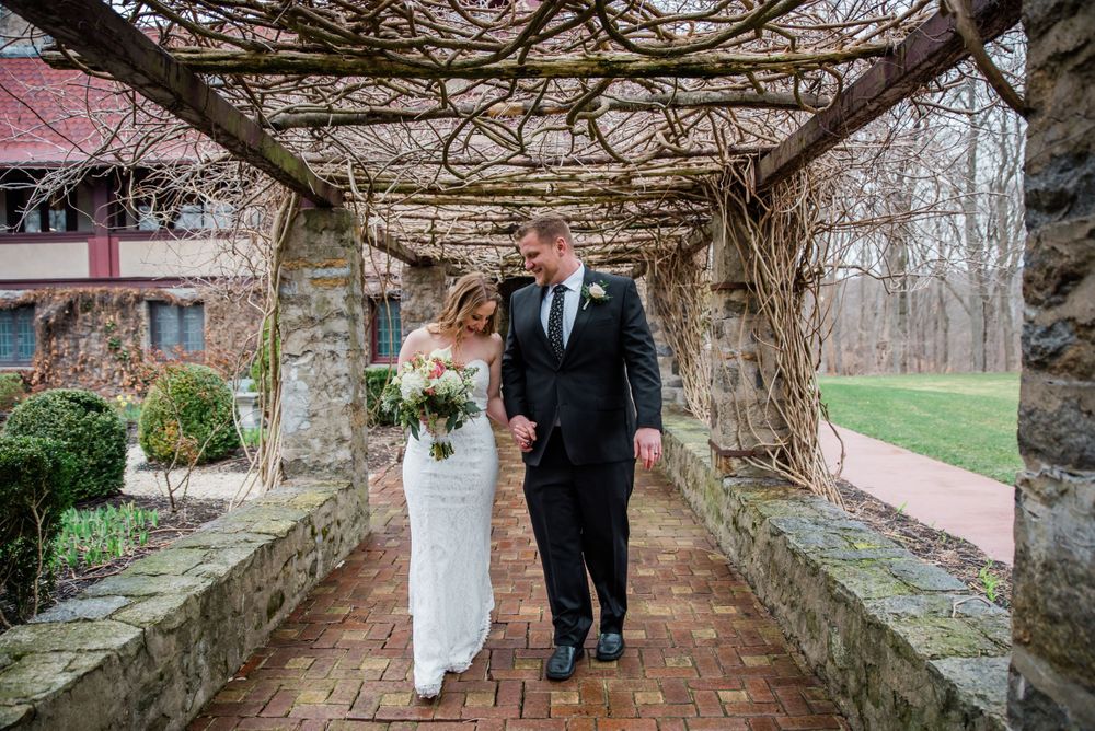 A romantic wedding photo captured under a vine-covered stone pergola with red brick pathway.