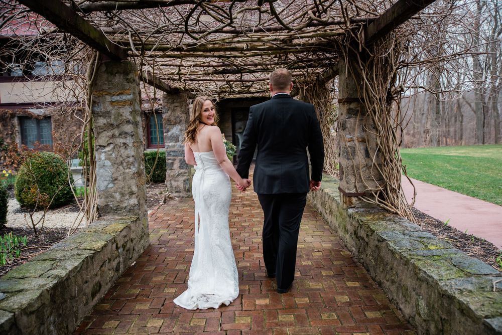 Newlyweds walk away hand in hand beneath rustic stone arbor covered in vines.