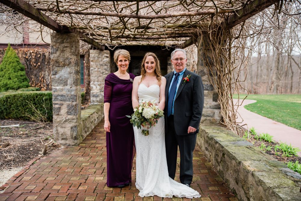 Family wedding portrait under rustic stone pergola with vines and brick flooring.
