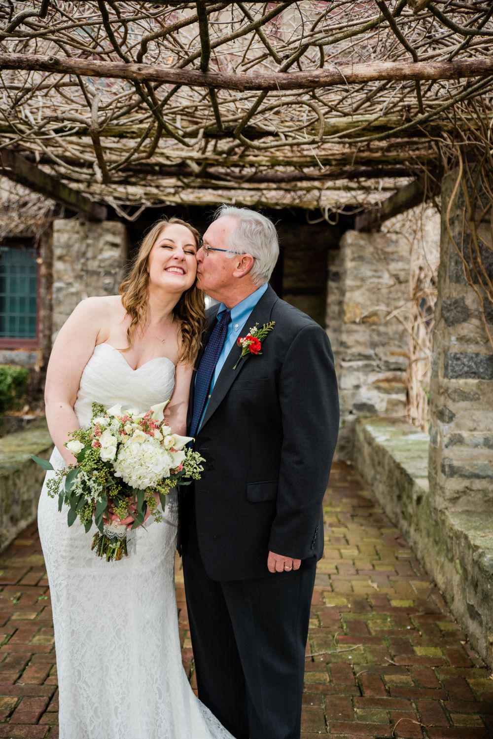 Tender wedding moment captured under stone archway with vines overhead.