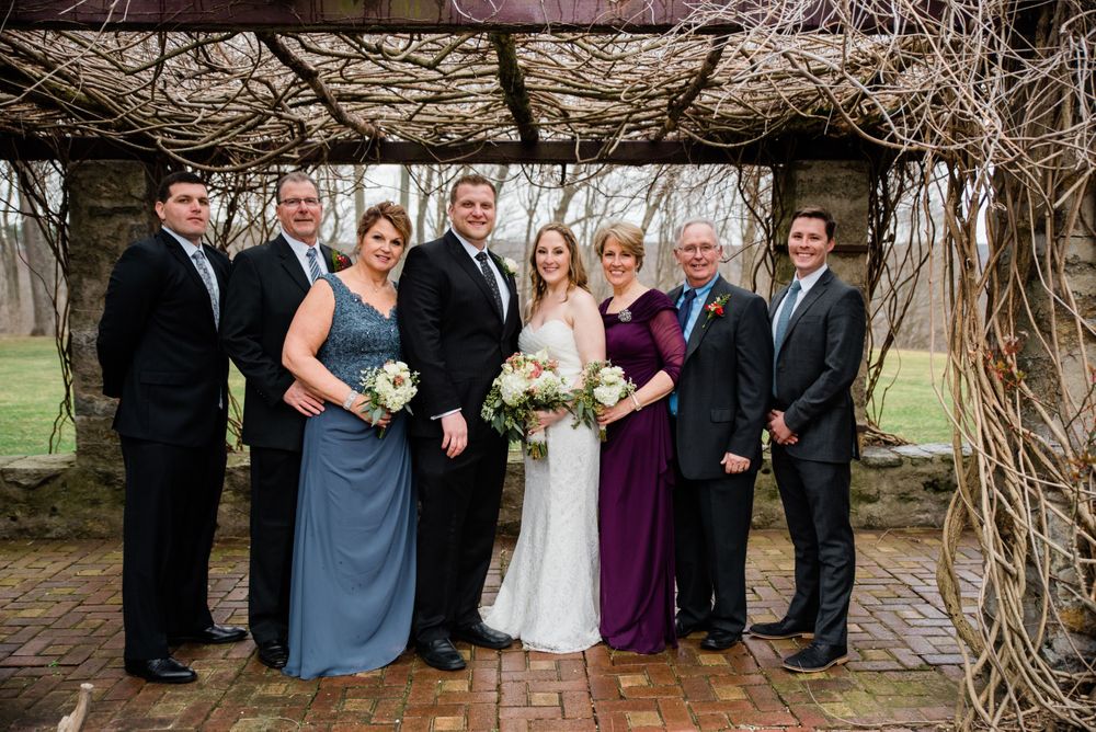 Wedding party poses together under an archway with stone walls and climbing vines.