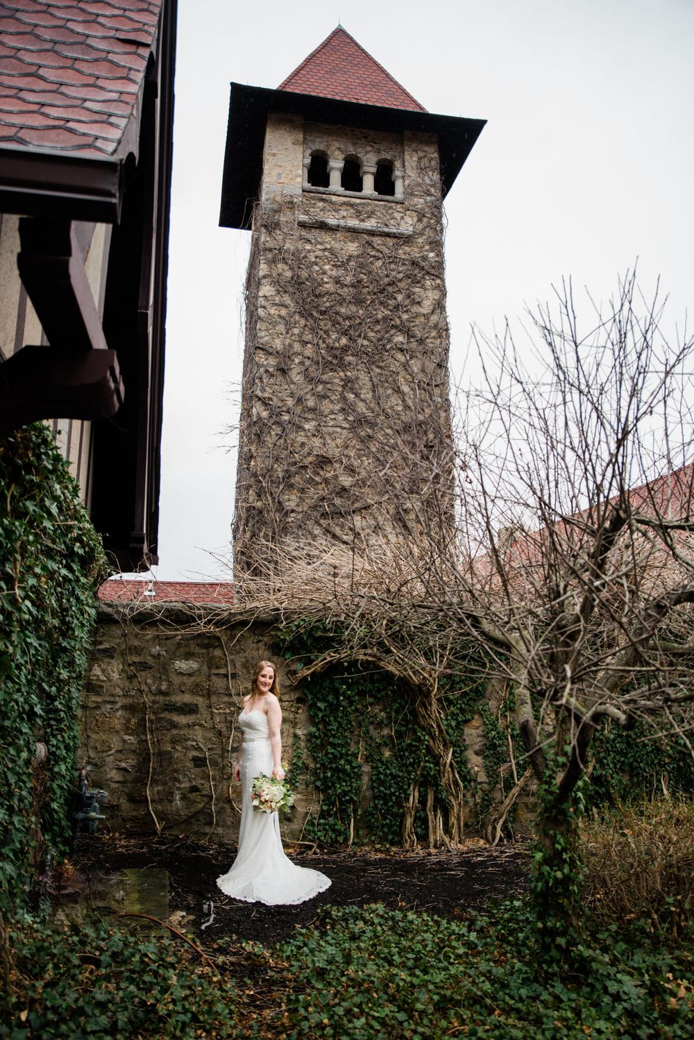 A white wedding dress stands out against stone tower and ivy-covered walls in winter garden setting.