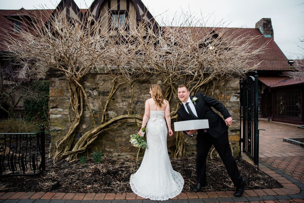 Playful wedding photo against Tudor-style architecture with bare winter branches.
