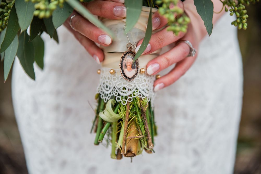 A vintage-style cameo brooch adorns a wedding bouquet wrapped in white lace and greenery.