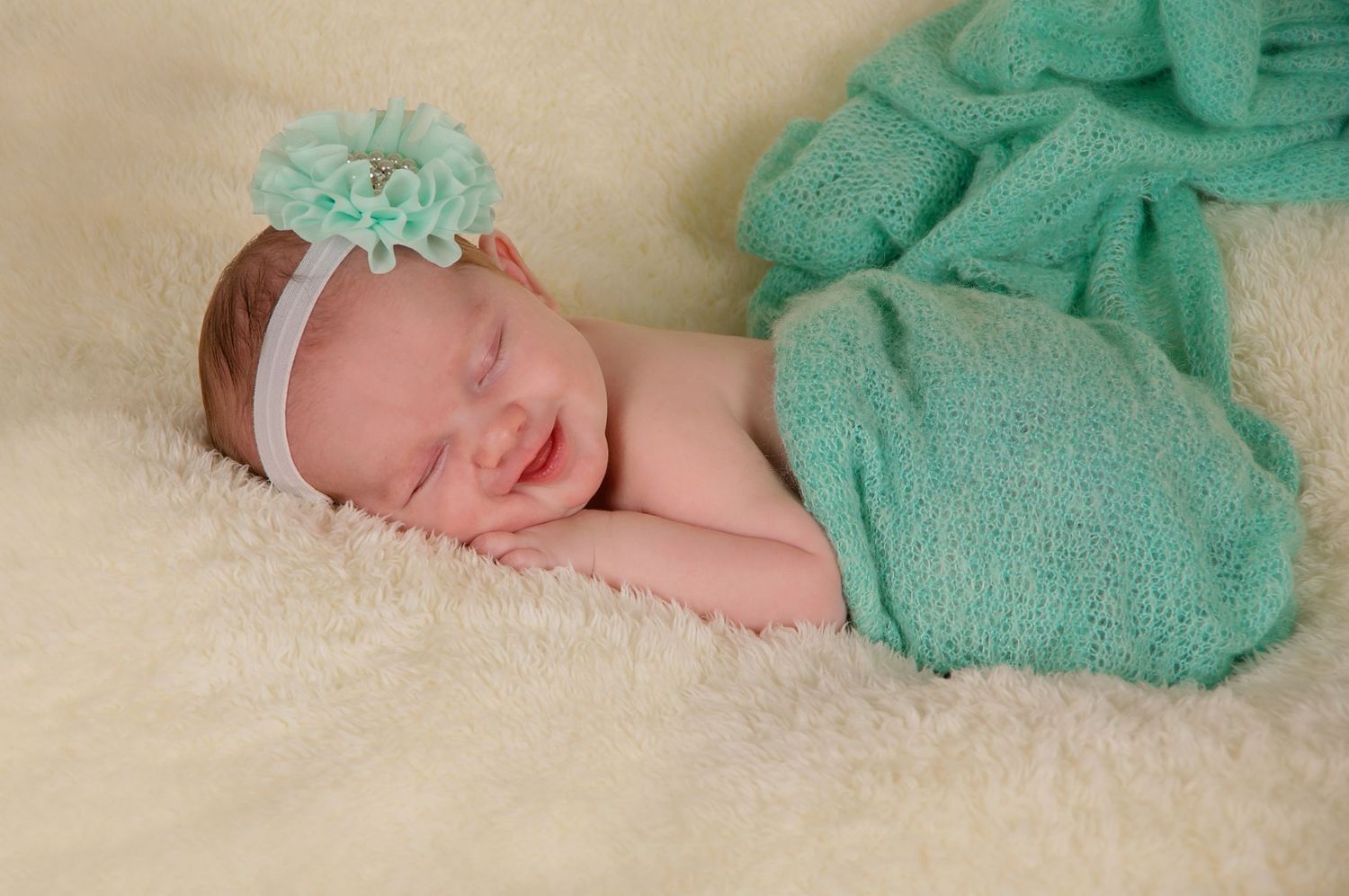 newborn photography of baby girl sleeping on her tummy wrapped in mint on fluffy blanket