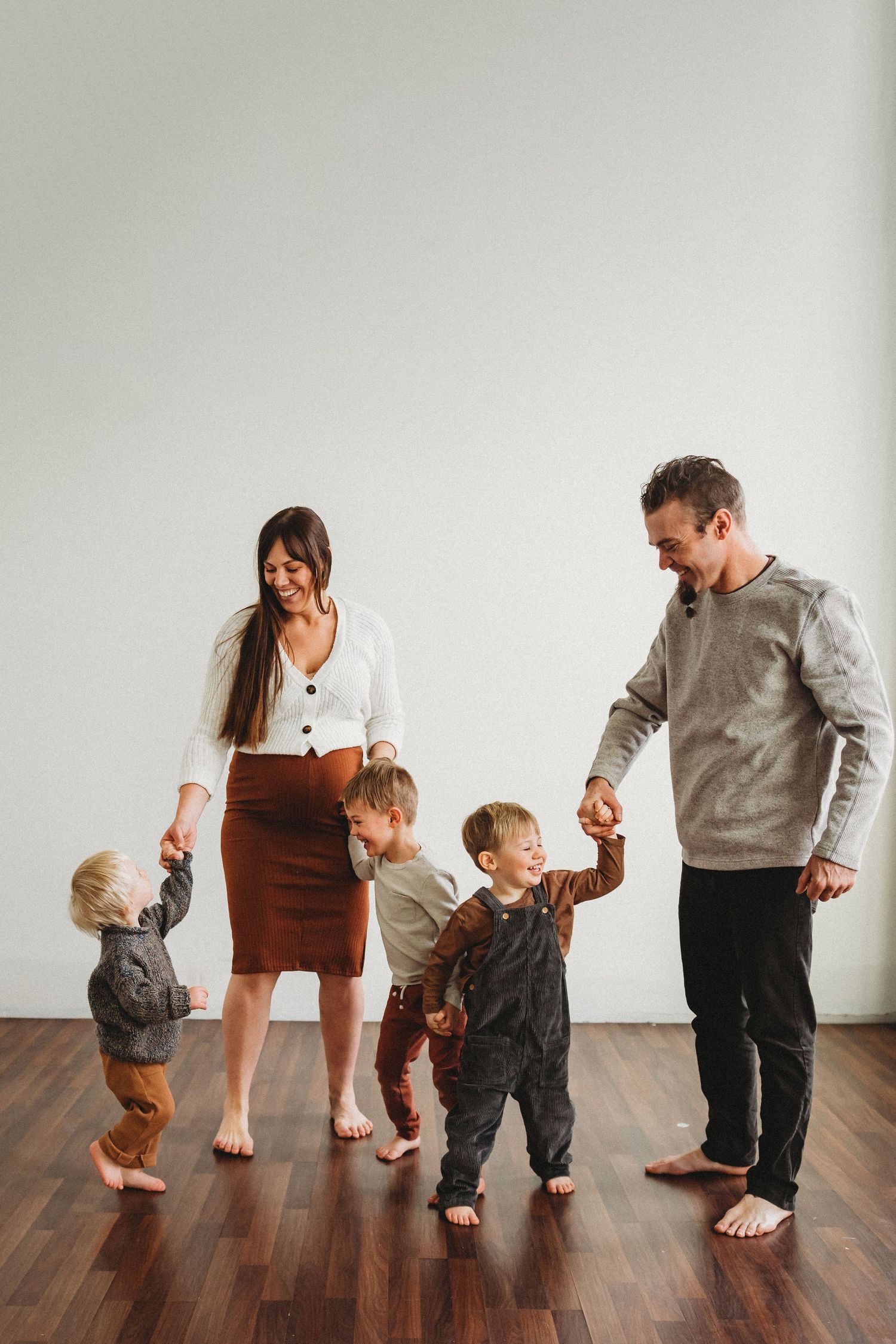 Family walking together and holding hands on hardwood floor in minimalist setting.