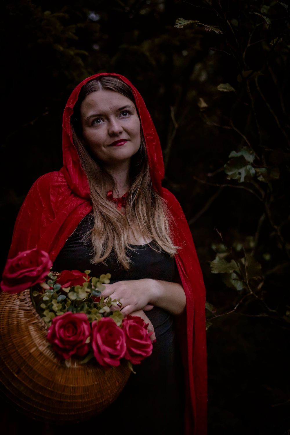 Modern Little Red Riding Hood interpretation with basket of roses in forest setting.