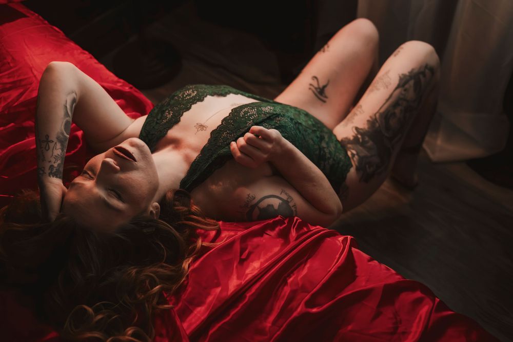Artistic boudoir photo featuring dark red fabric and green lingerie in moody lighting.