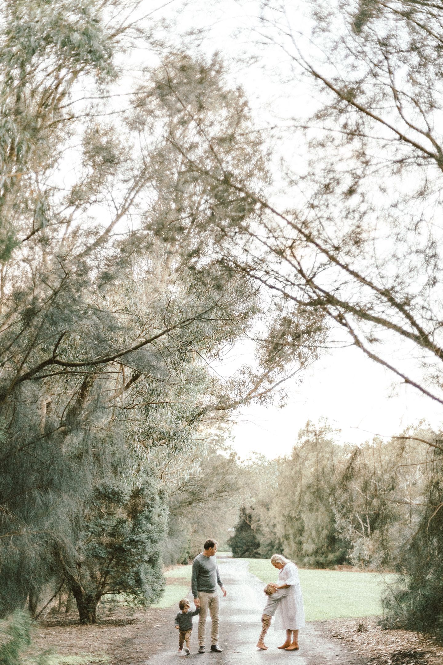 A family walking together on a winding path through trees during a golden sunset photo session.