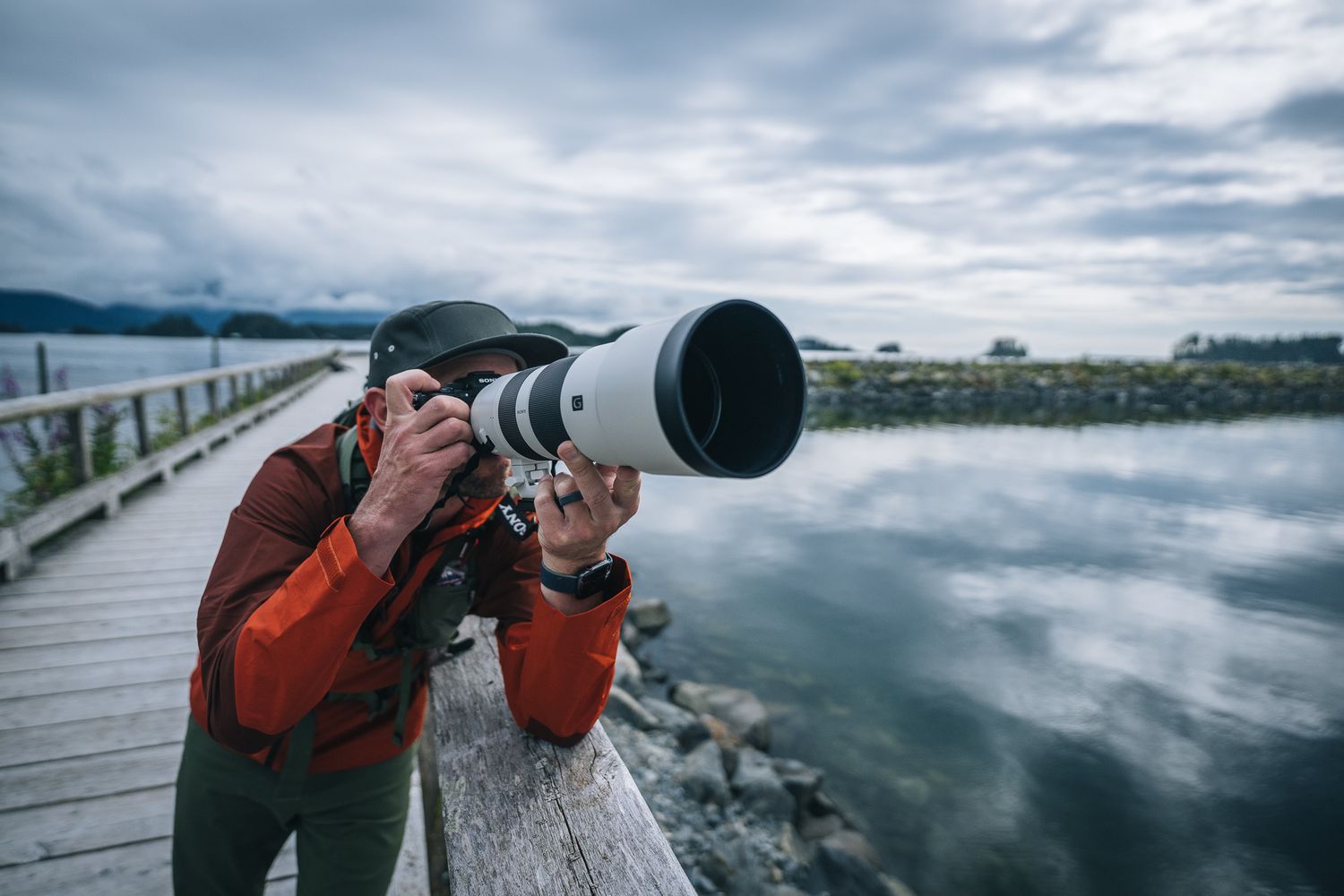 Wildlife photographer with large telephoto lens shooting from wooden pier over misty water.