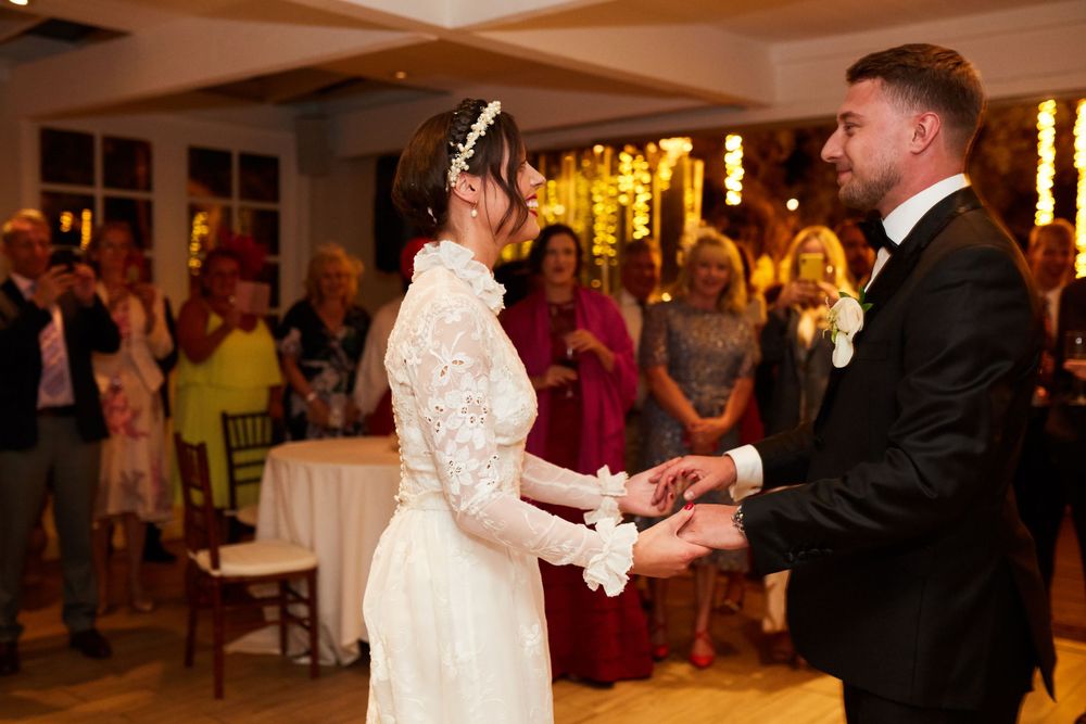 Wedding couple shares their first dance surrounded by guests in an elegant indoor venue.