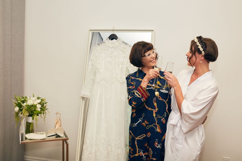 Two people sharing a tender moment while getting ready in a dressing room with a wedding gown visible.