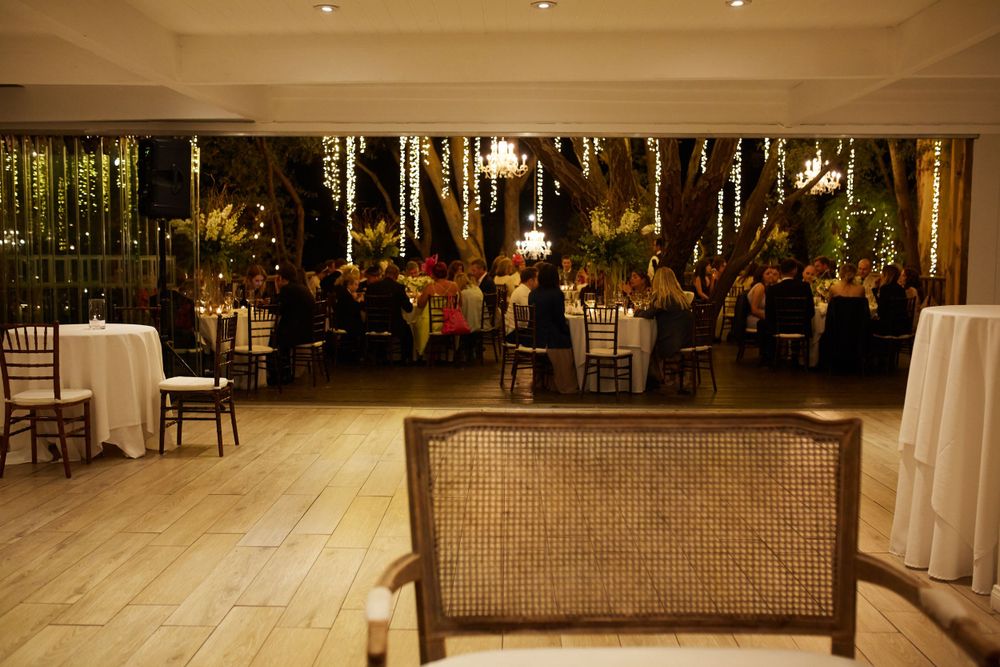 Warm ambient lighting illuminates an indoor wedding reception with elegant table settings.