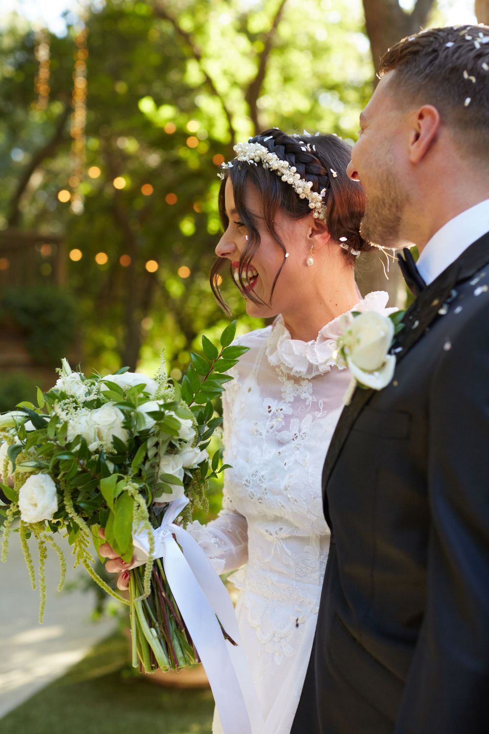 A couple shares a romantic moment outdoors with the bride holding a lush white floral bouquet.