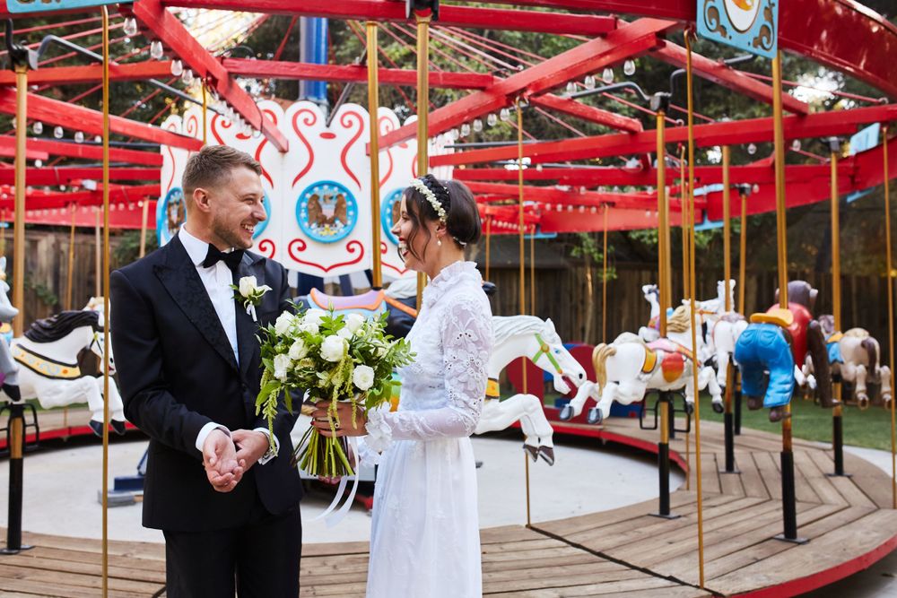 A wedding couple stands in front of a vintage carousel with bright red beams.