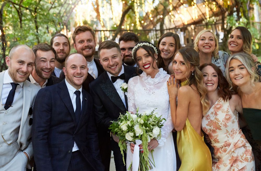 Wedding party poses together outdoors with colorful attire and floral bouquets.