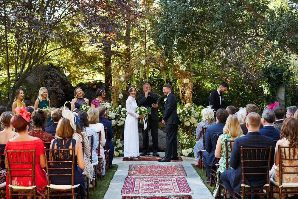 Wedding ceremony in progress with guests seated on wooden chairs along a Persian rug aisle runner.