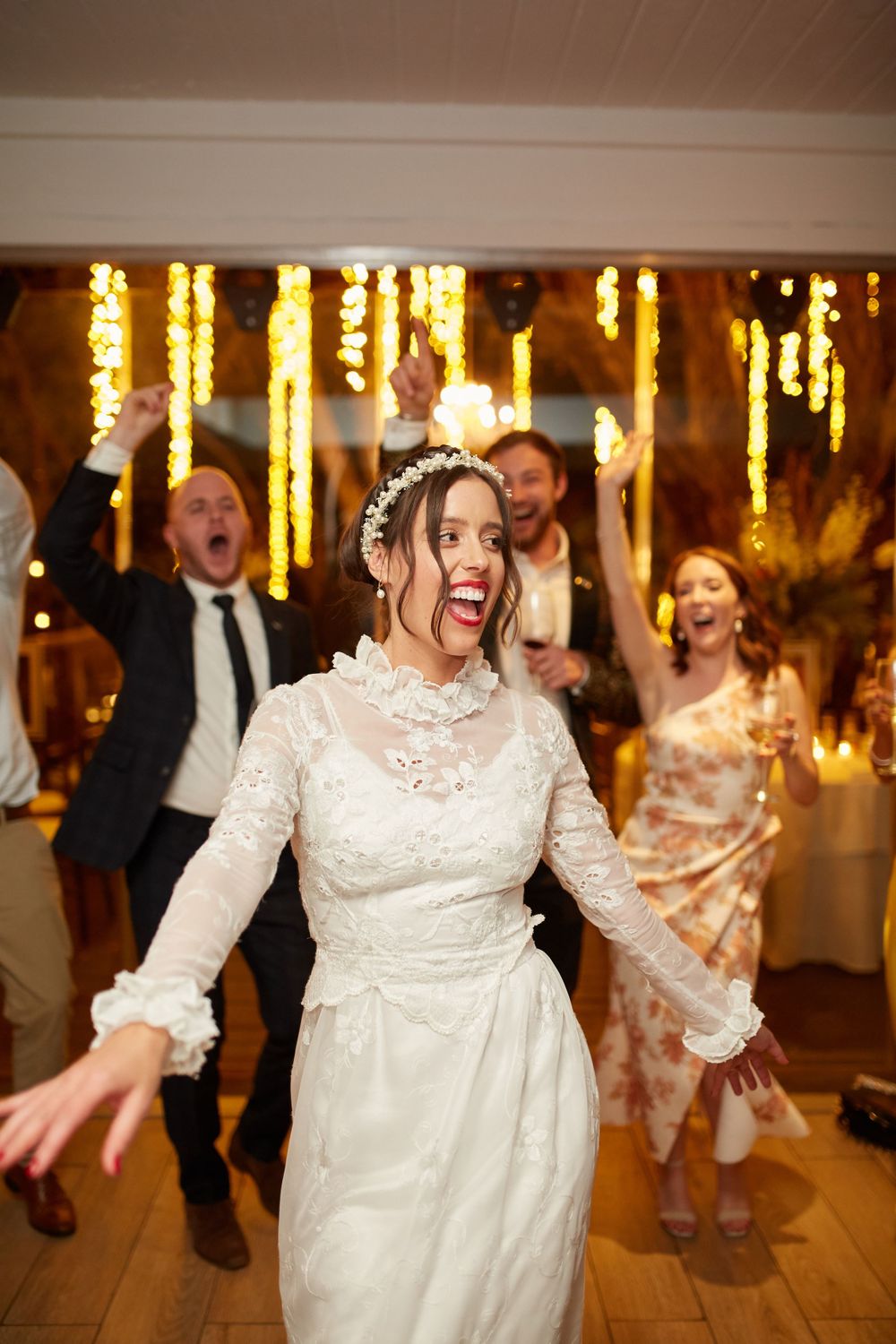 Candid celebration moment on the dance floor with guests and string lights in background.