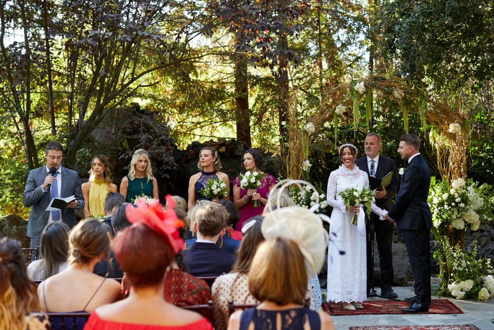 Outdoor garden wedding ceremony with guests seated on wooden chairs watching the proceedings.