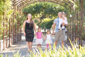 Family of five holds hands and smiles under an arched tunnel of roses with decorative grass framing the front.