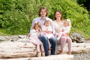 Family of five sits on a log framed by trees as the little girls giggle and squirm.