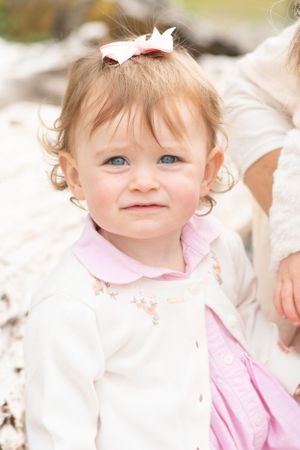 little girl with a pink bow on top of her head looks right into the camera with sparkling blue eyes