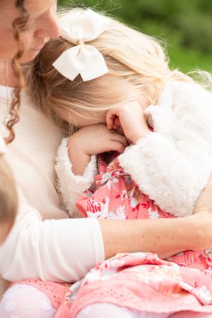 little one sits on mom's lap rubbing eyes and getting comfort. Mom is leaning in talking softly to her.