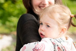 little toddler looks off to the side while sitting on mom's hip while mom lovingly smiles at the little one.