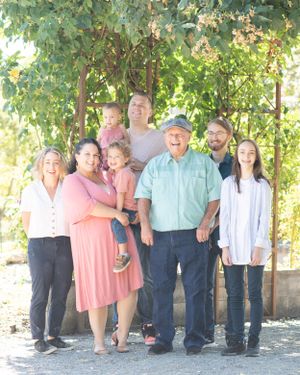 Grandpa stands for a portrait with his grandkids and great grandkids under an arching tunnel of roses.