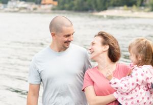mom looks back and laughs over her should at her husband while holding their little girl on her hip at the beach shore.
