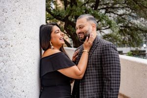 Happy couple laughing and sharing a tender moment leaning against a pillar outdoors.