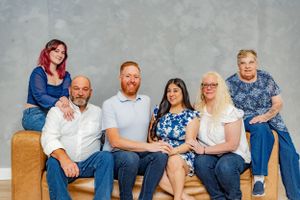 Happy family of six posing together on a couch against a gray backdrop in casual blue jeans outfits.