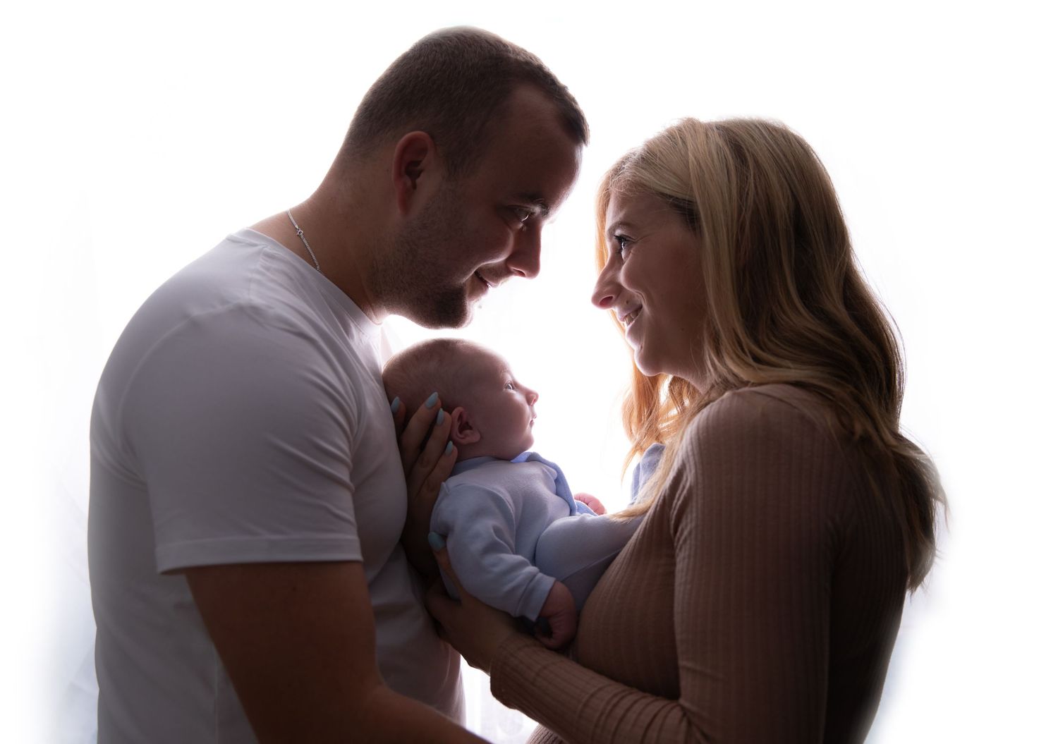 Silhouette portrait of new parents holding their baby against bright window.