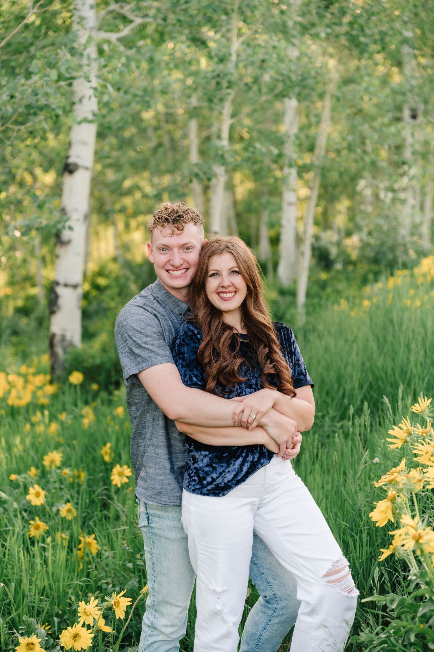 A couple embraces in a meadow filled with yellow wildflowers and aspen trees.