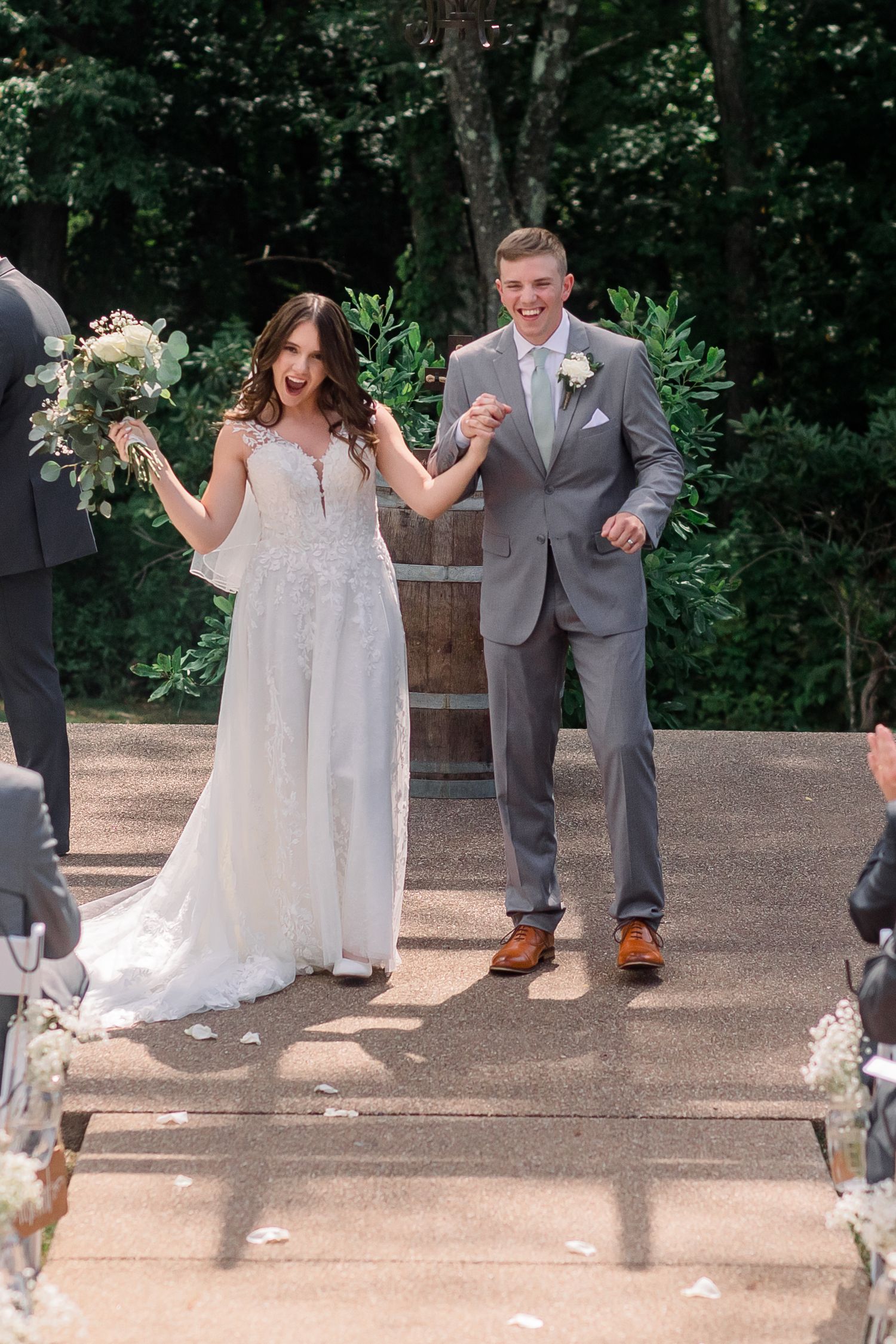 Wedding party celebrates with joy at outdoor ceremony site decorated with rustic barrels and flowers.