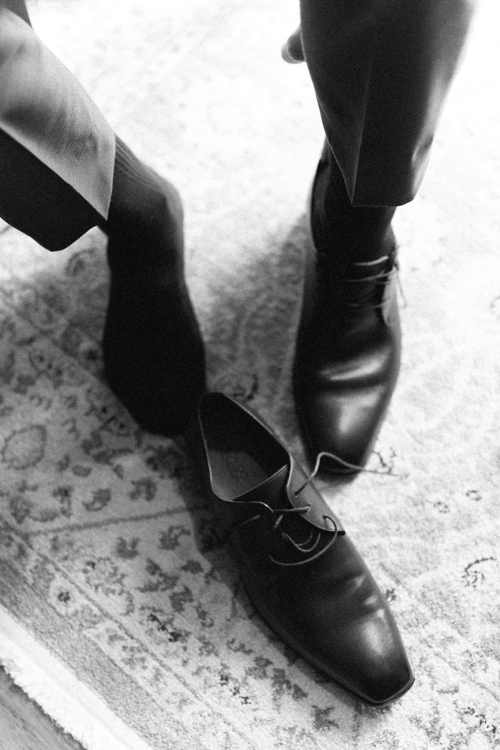 Black and white photo of formal leather dress shoes on patterned carpet.