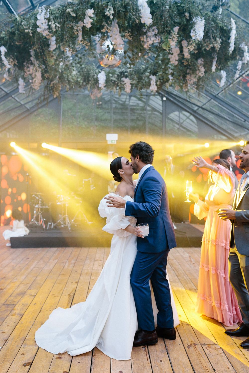 Couple sharing intimate dance moment under hanging floral decorations and golden lights.