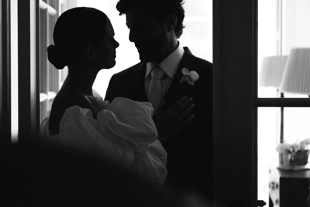 Romantic silhouette of a couple embracing in black and white with dramatic window lighting.