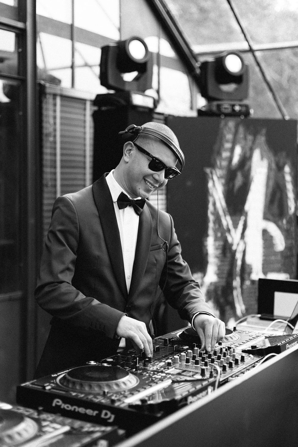 DJ in formal attire and cap performs at wedding reception using Pioneer equipment.