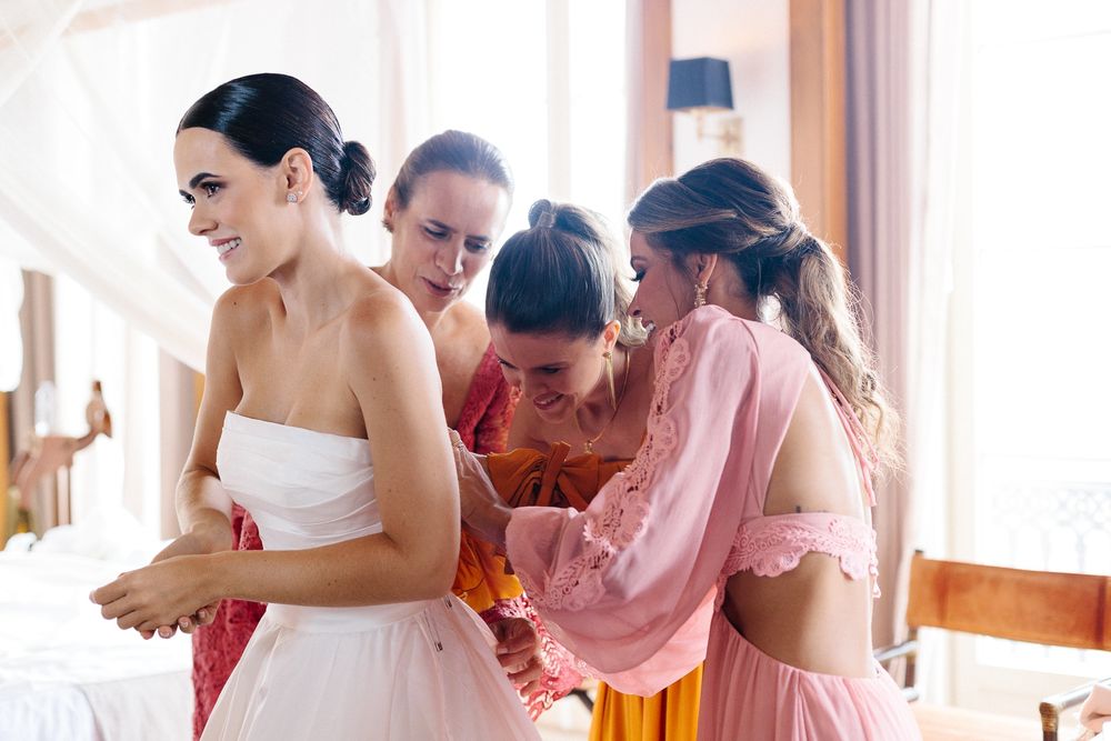 Bridal preparation scene with women in pink and white dresses helping with final touches.