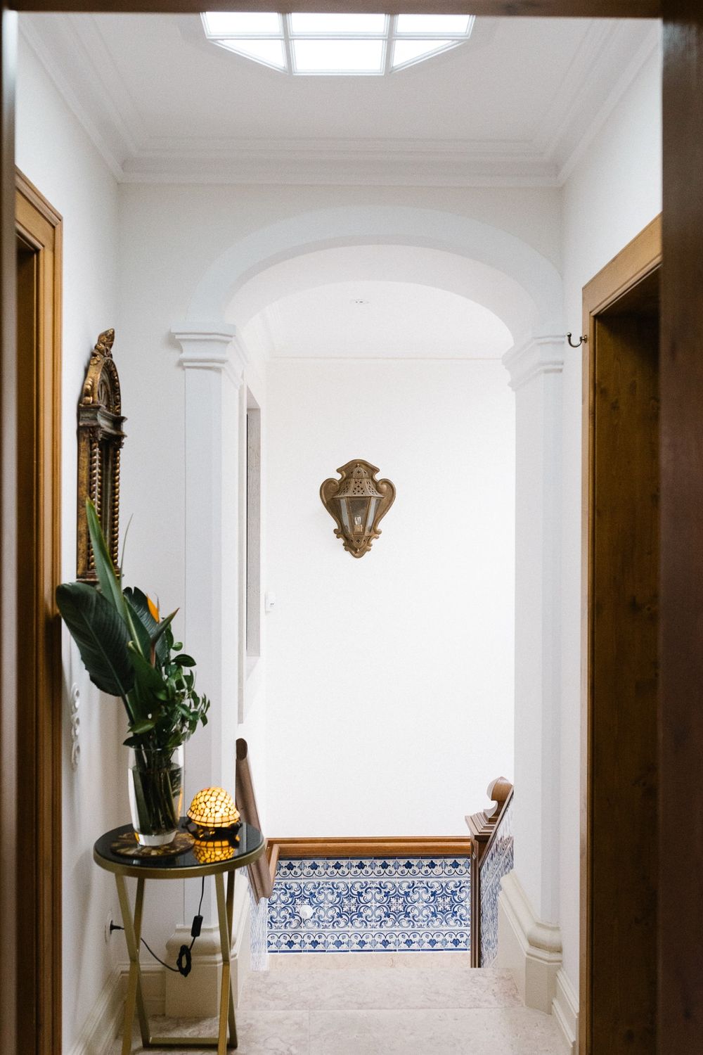 White hallway with arched doorway featuring decorative wall mount and potted plant.