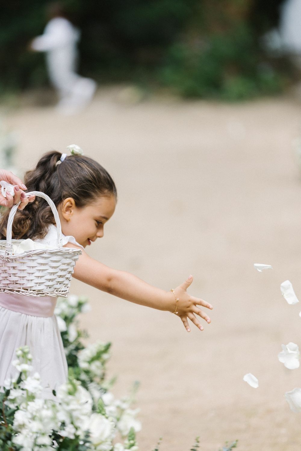 Young flower girl in white dress playfully tosses petals in a garden setting.