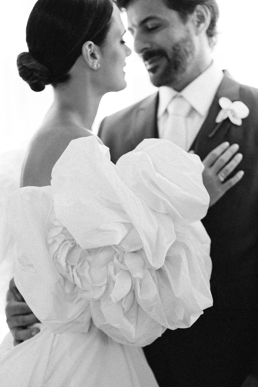 Elegant bride in dramatic puff sleeve wedding dress embraces groom in intimate black and white portrait.