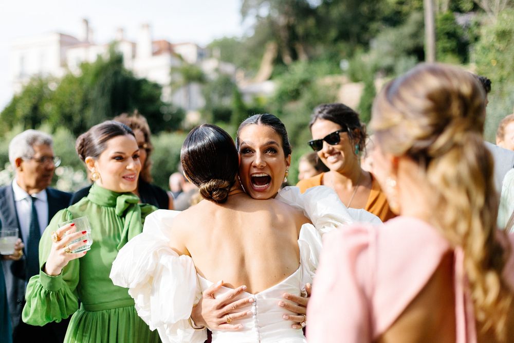 Wedding guests in colorful dresses celebrate and embrace during outdoor reception.