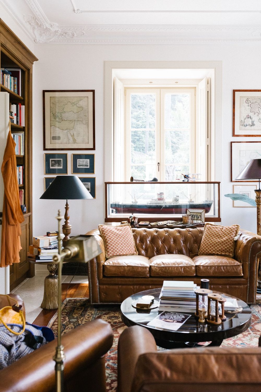 Cozy living room with leather Chesterfield sofa, vintage decor, and natural light from tall windows.