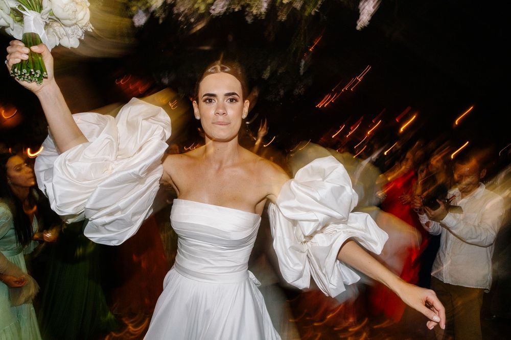 A celebratory dance moment captured in a white dress with dramatic sleeves.
