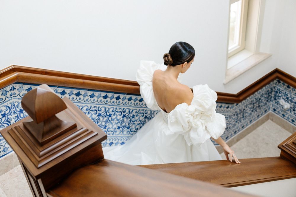 Gorgeous wedding dress with dramatic bow detail shown on an ornate staircase with blue patterned tiles.