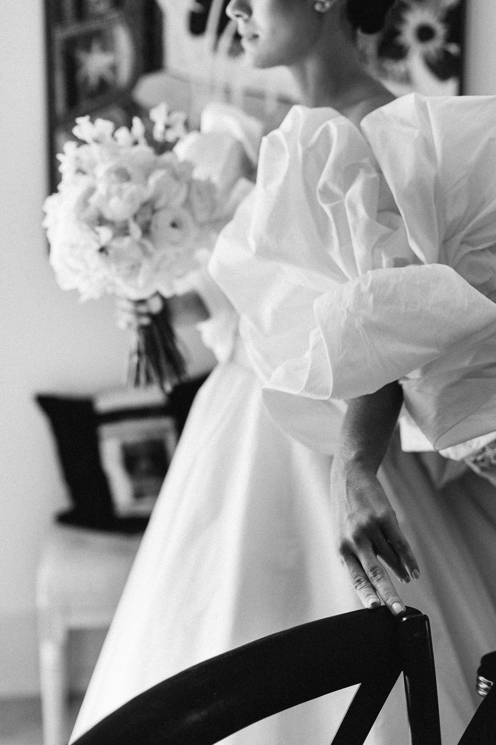 Black and white detail of wedding dress with oversized sculptural bow and floral bouquet.