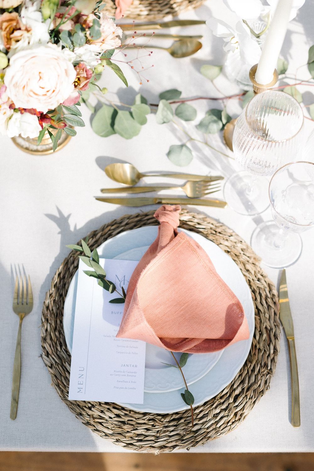 Wedding place setting with coral napkin, woven charger, and delicate floral centerpiece.